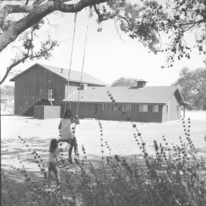 Girls on swing next to Old Meadows Center, where the Rothschild barn was relocated to be the new park center building.  Donated by photographer Herb Noseworthy.